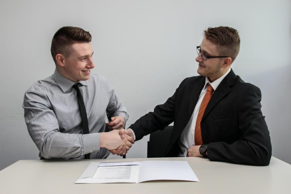 two men facing each other while shake hands and smiling in front of agreement